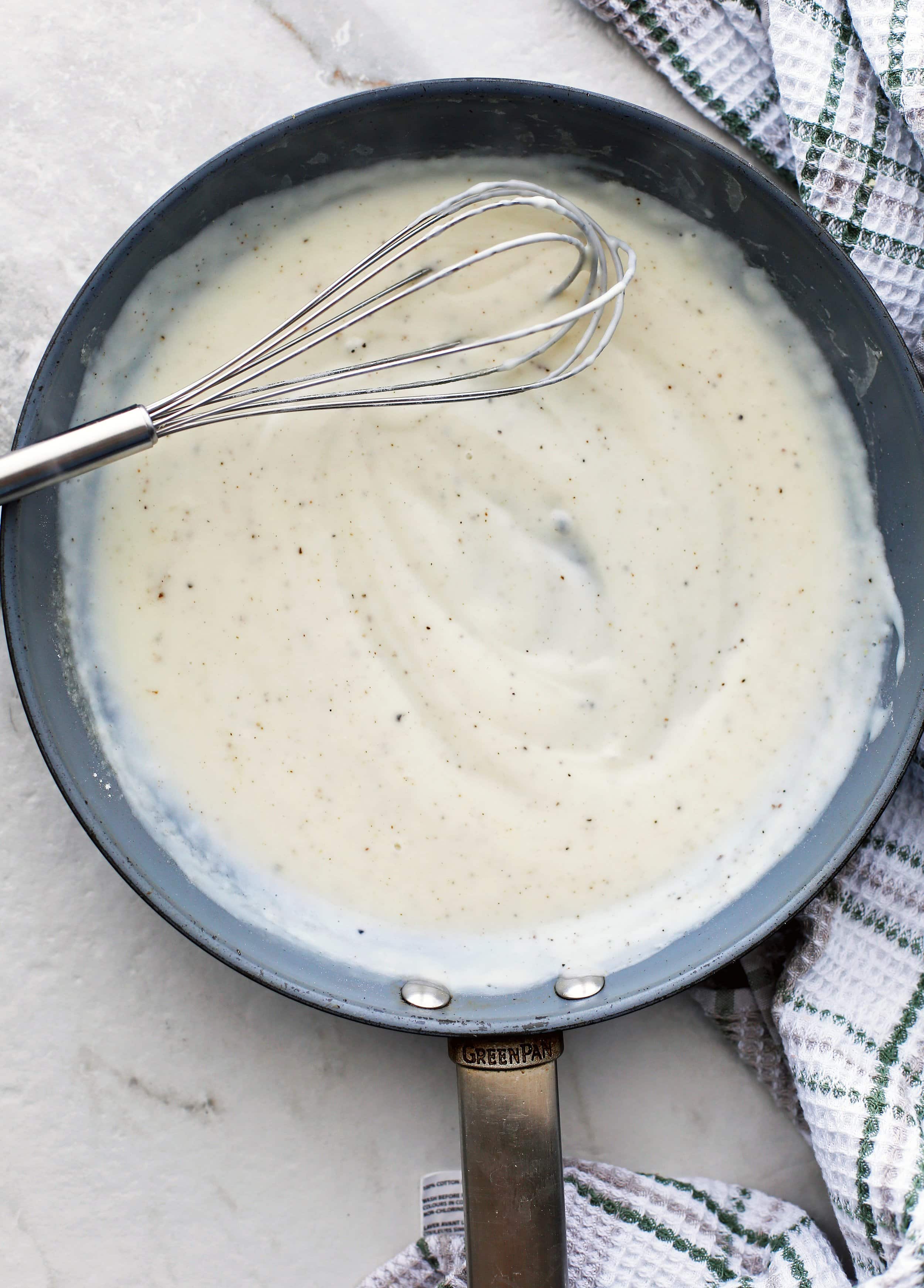 White sauce also known as béchamel sauce in skillet with a metal wired whisk.