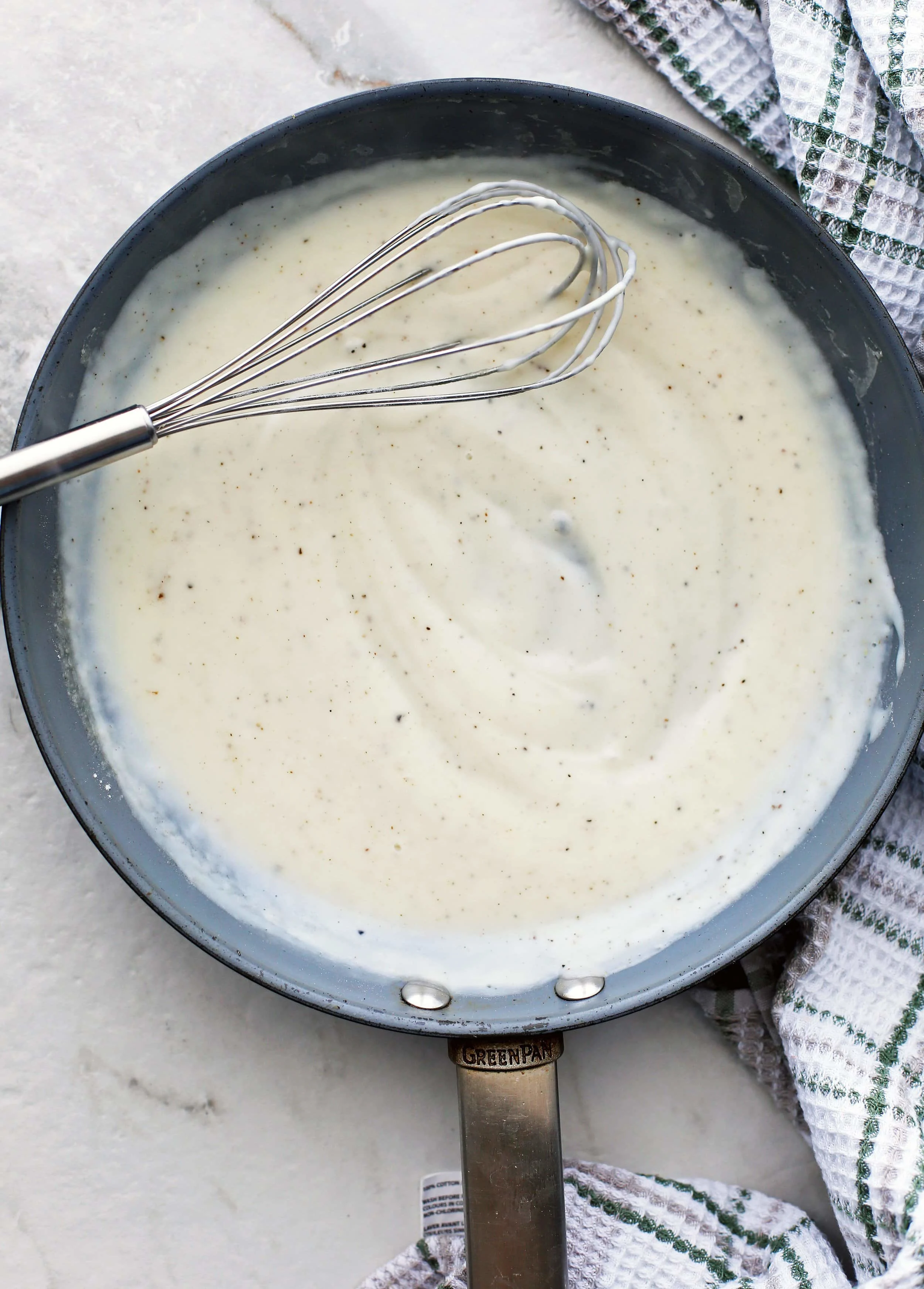 White sauce also known as béchamel sauce in skillet with a metal wired whisk.