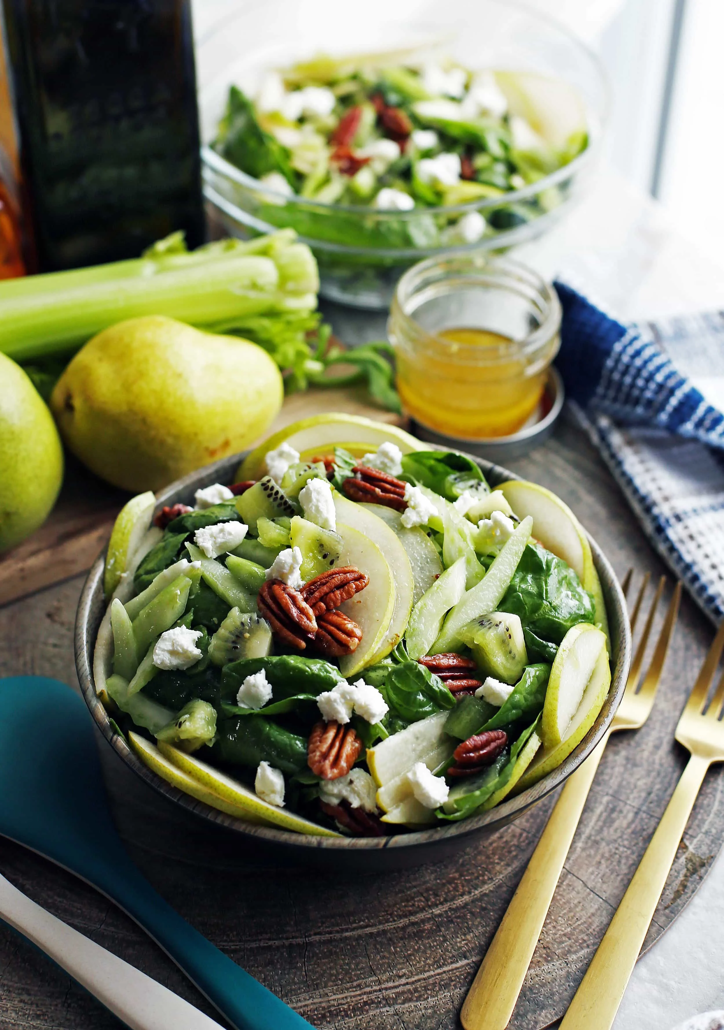 A bowl full of winter green spinach salad with pecans, pears, kiwi fruit, and pecans.