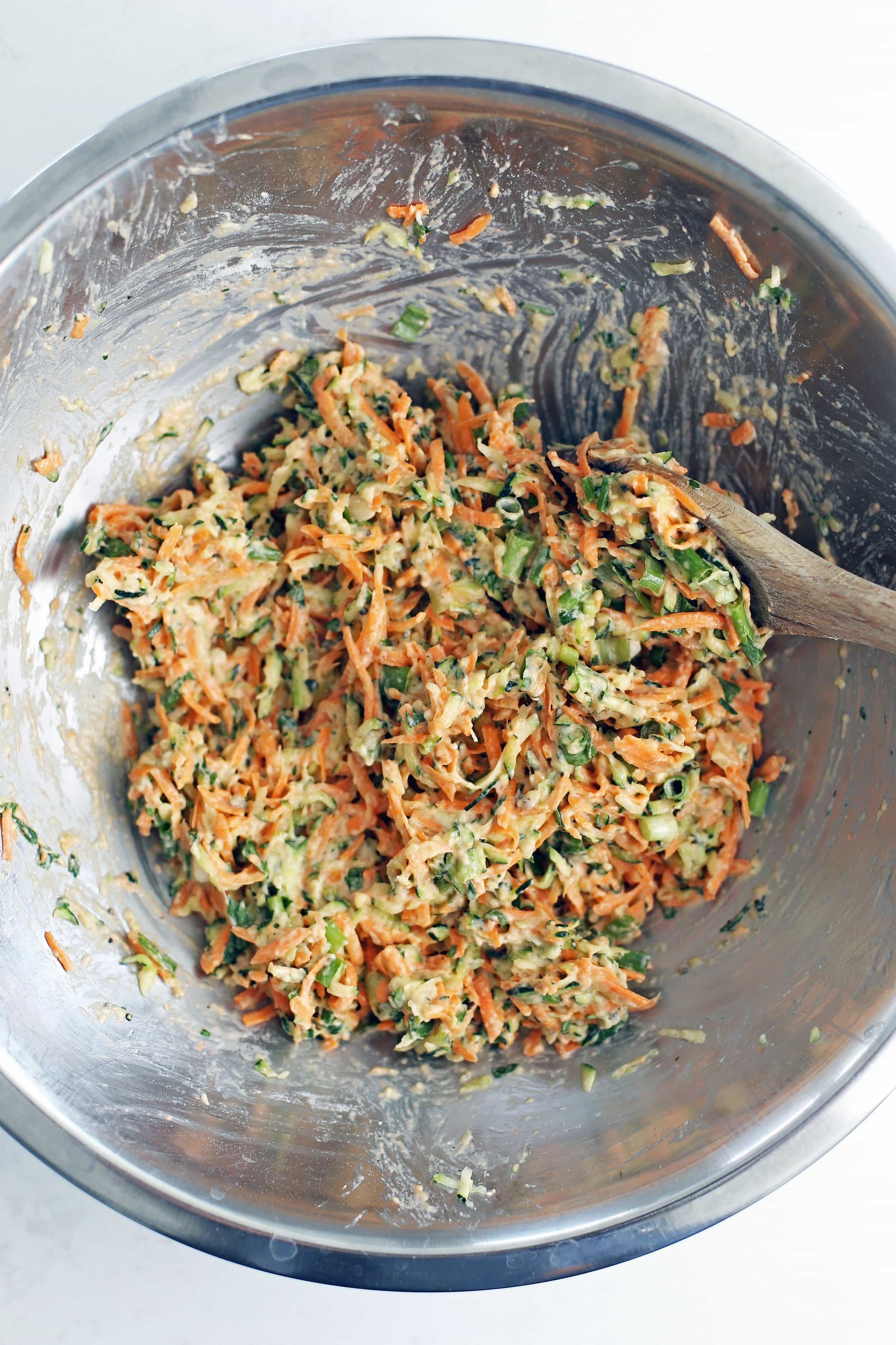 Zucchini carrot pancake ingredients combined together in a stainless steel bowl.