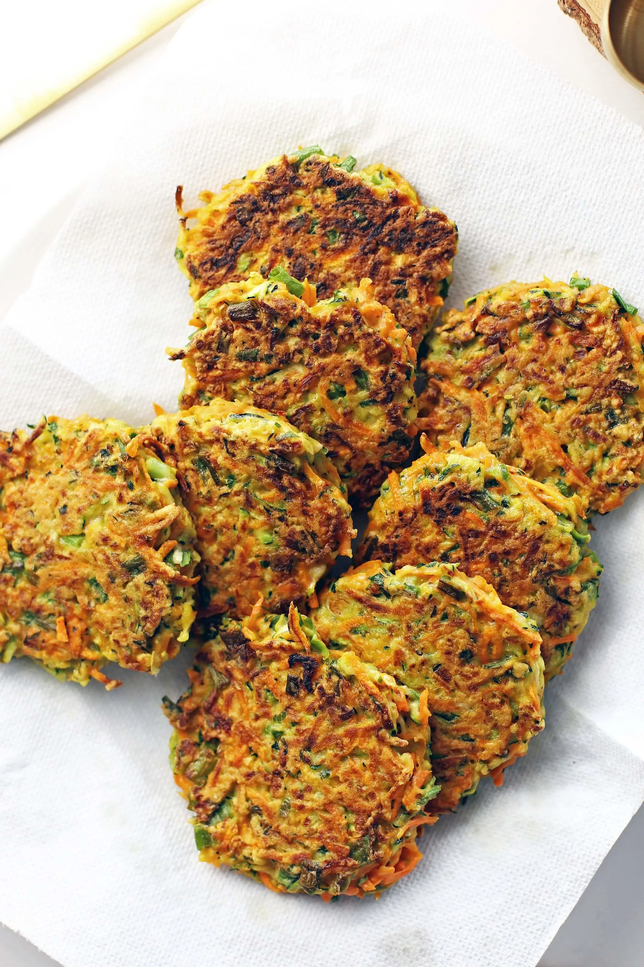Eight freshly fried zucchini carrot pancakes placed on a paper towel lined plate.