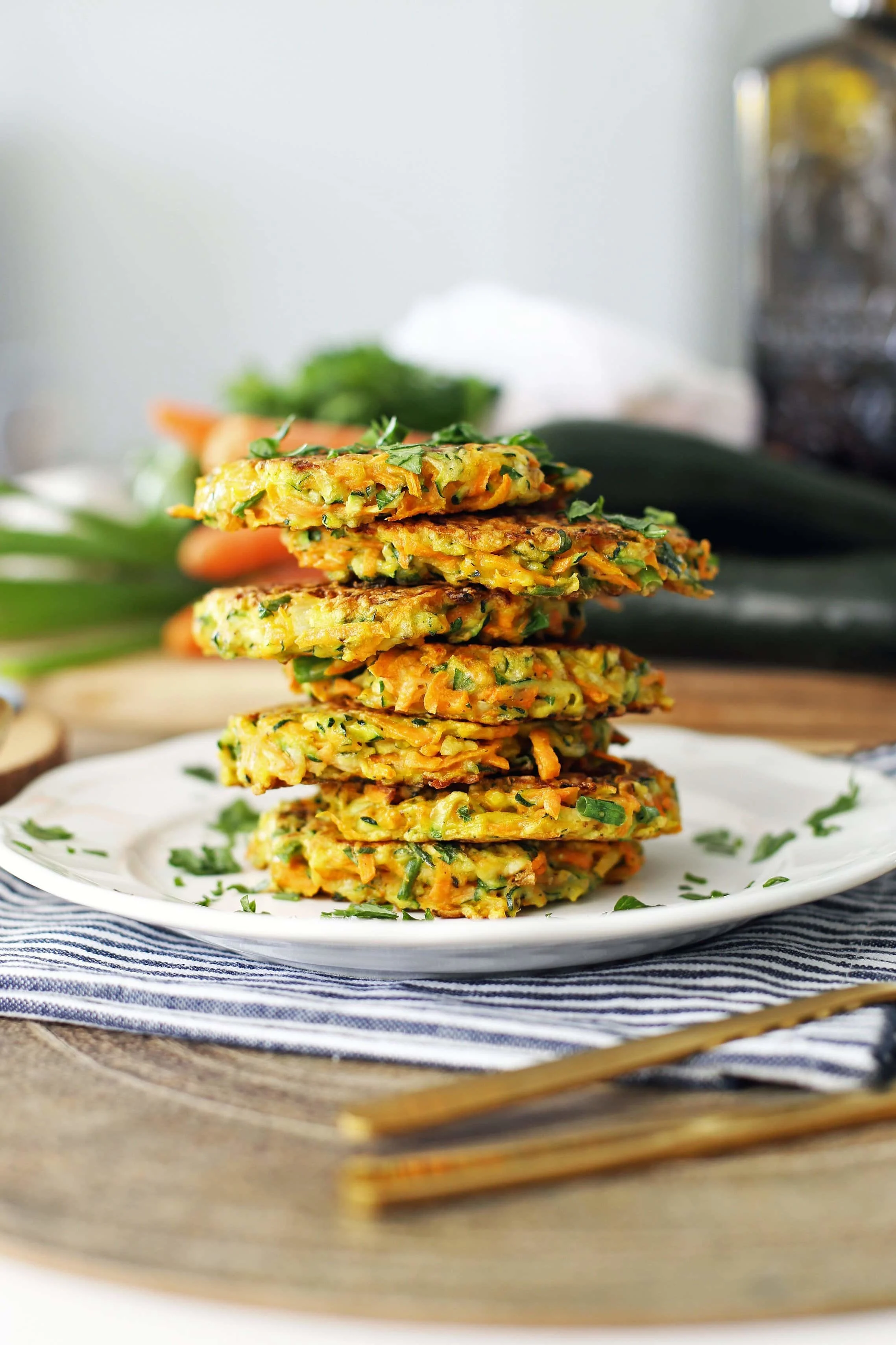 Seven zucchini carrot pancakes placed on top of one another and garnished with fresh parsley on a white plate.