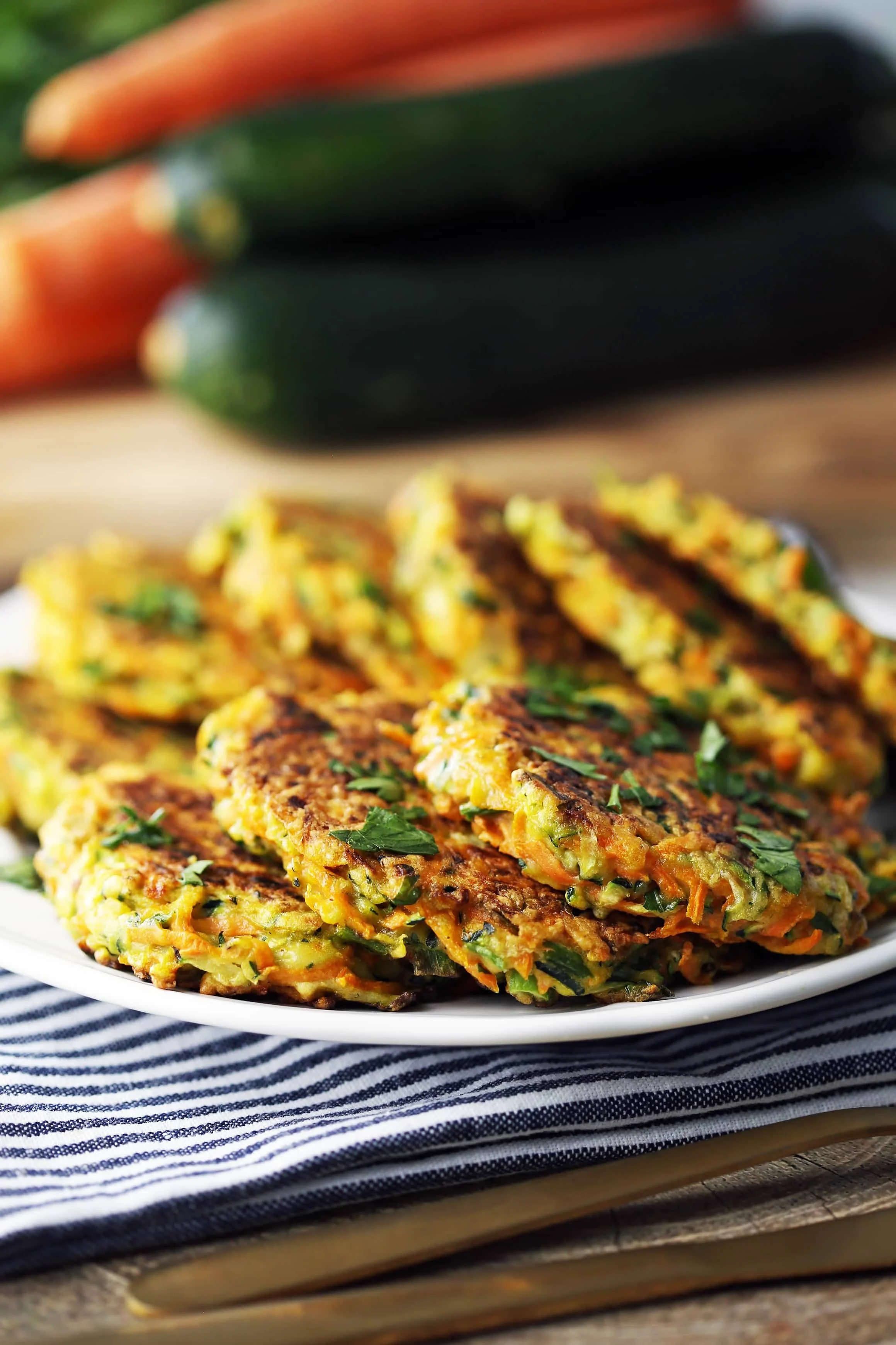 Seven zucchini carrot pancakes placed on top of one another and garnished with fresh parsley on a white plate.