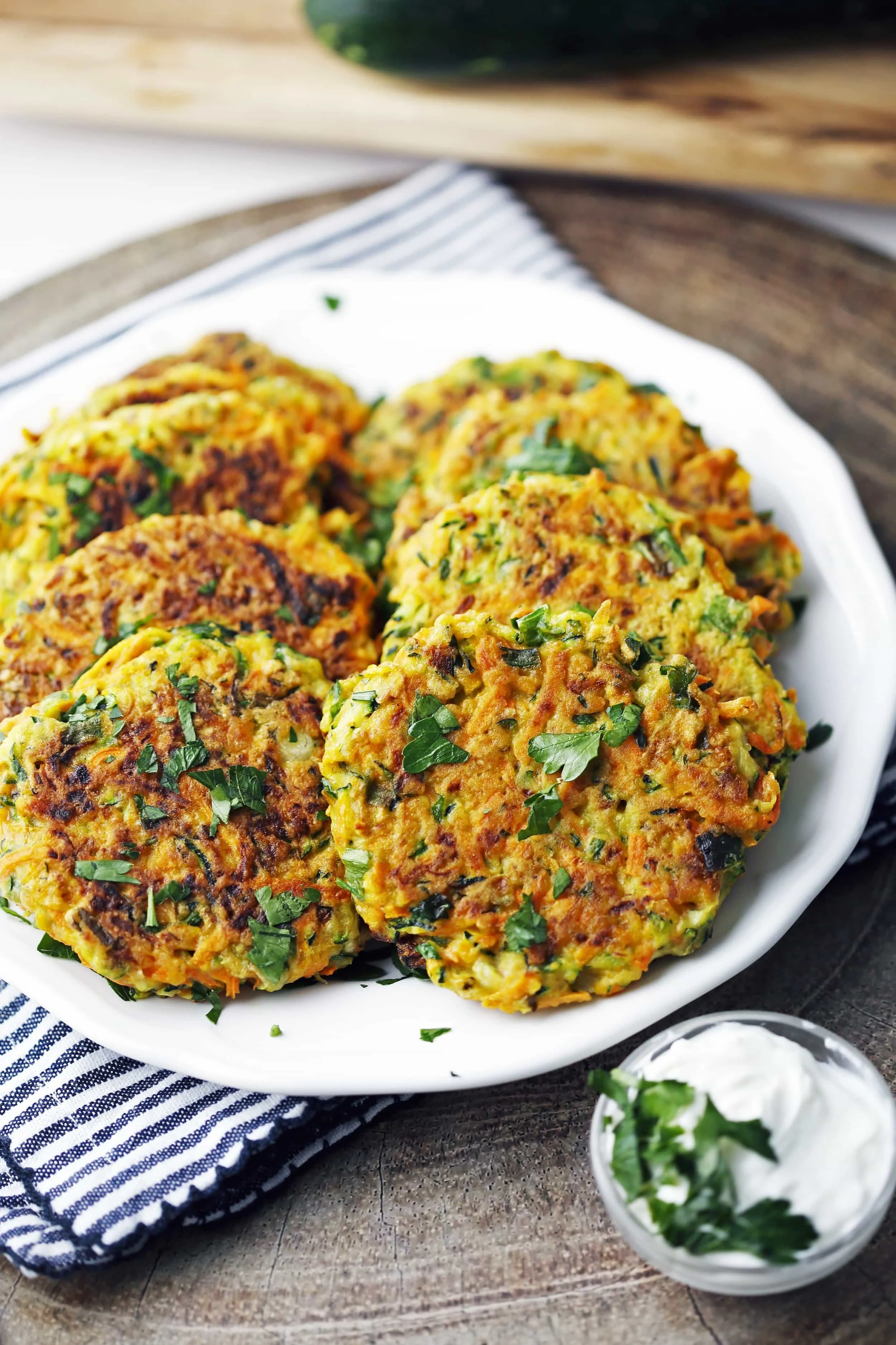 Eight zucchini carrot pancakes piled on a white place with plain Greek yogurt in a small glass bowl beside them.