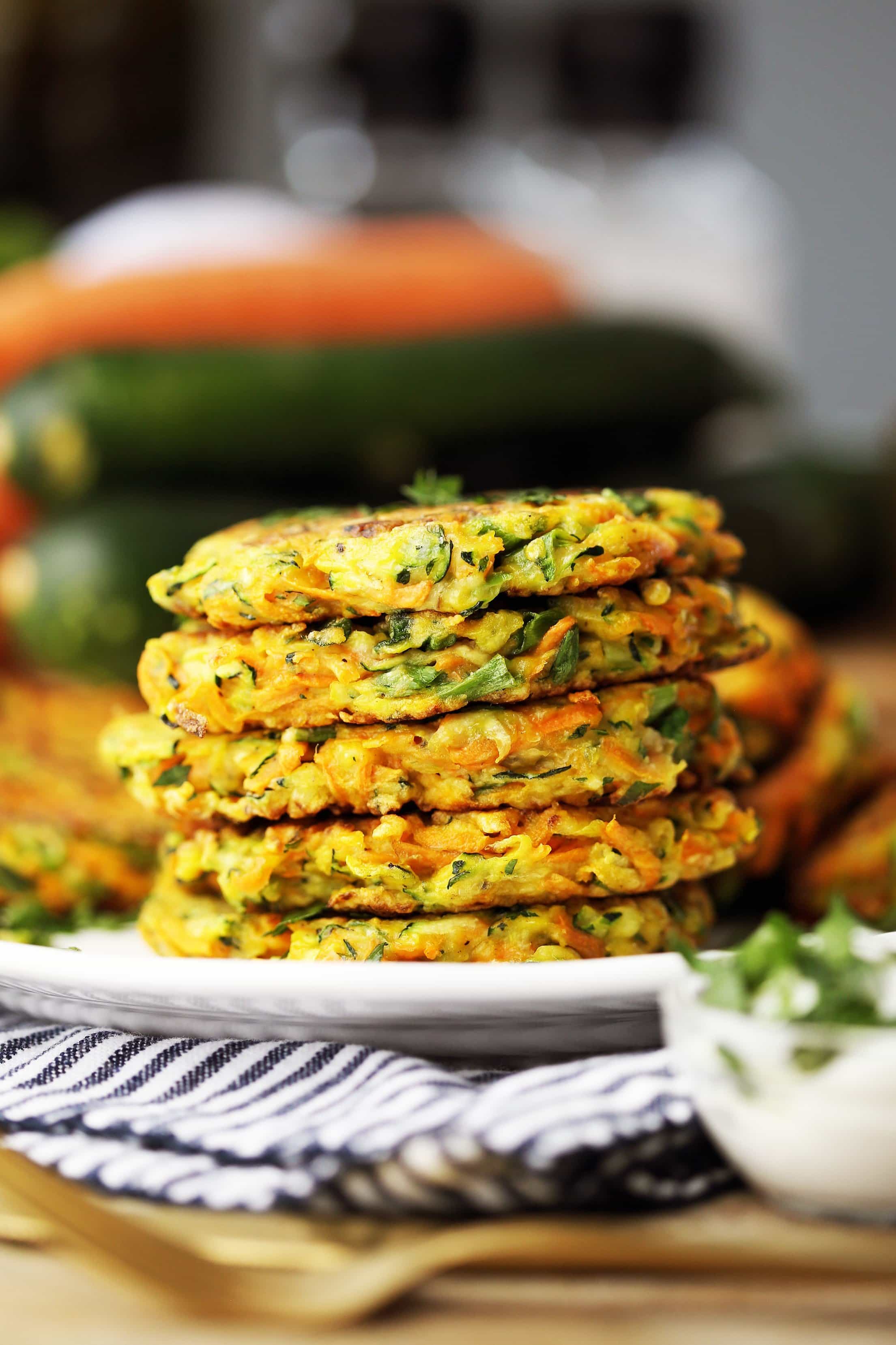 Five zucchini carrot pancakes stacked on a white plate with plain Greek yogurt in a small glass bowl on the side.