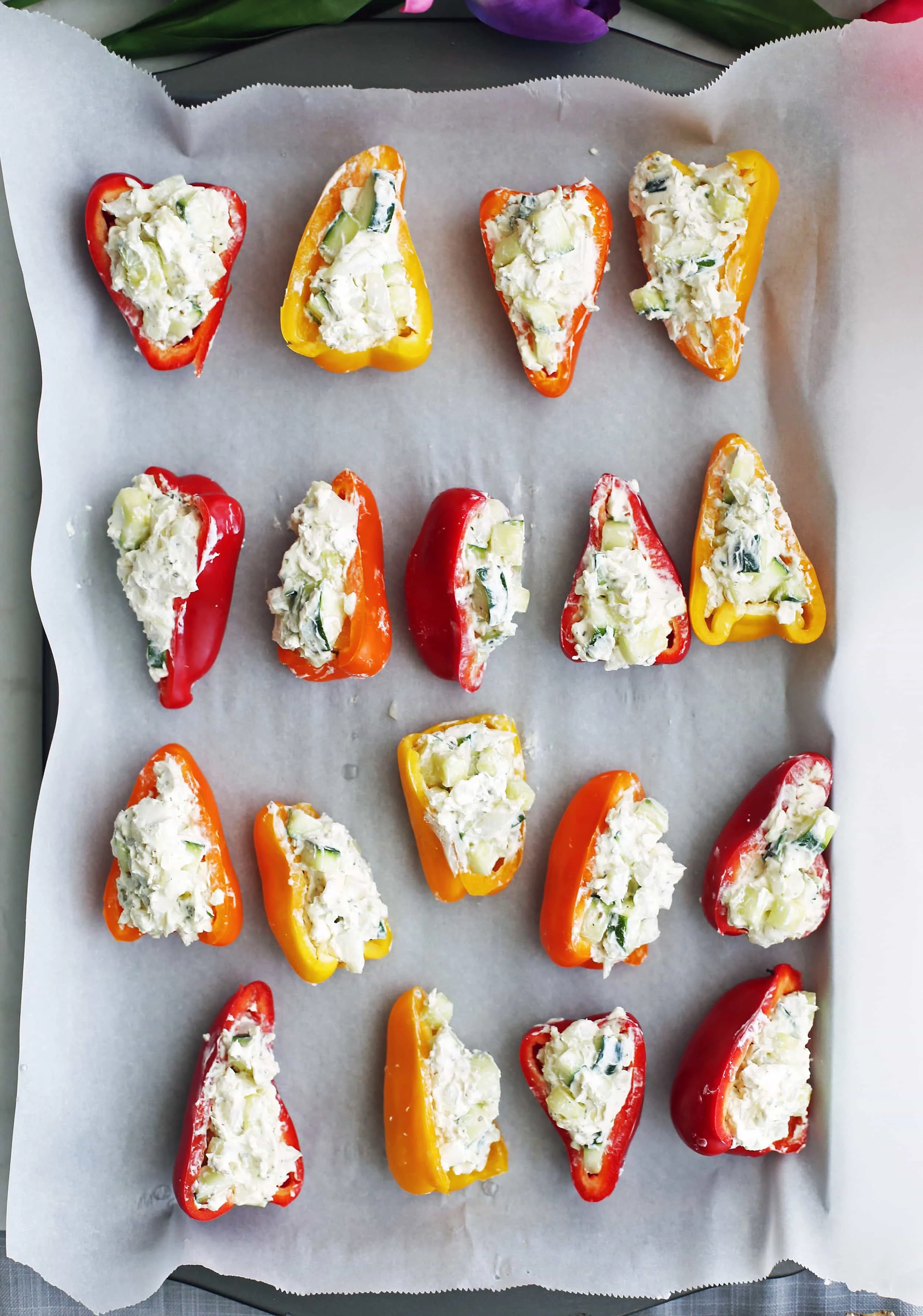 Zucchini and cream cheese mini stuffed peppers ready to be baked on a large baking sheet.