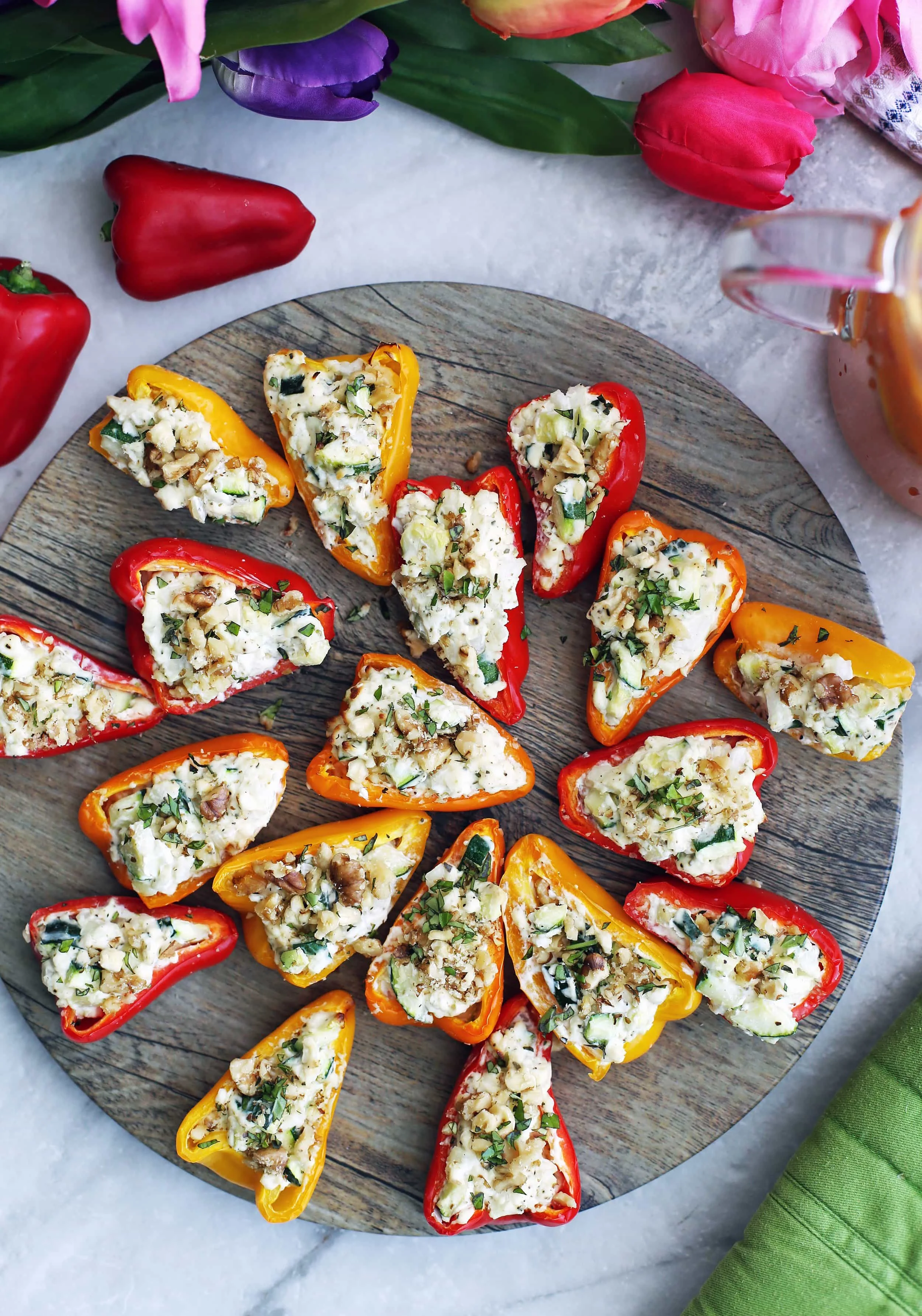 A round wooden platter filled with zucchini cream cheese mini stuffed peppers garnished wiith chopped walnuts and basil.