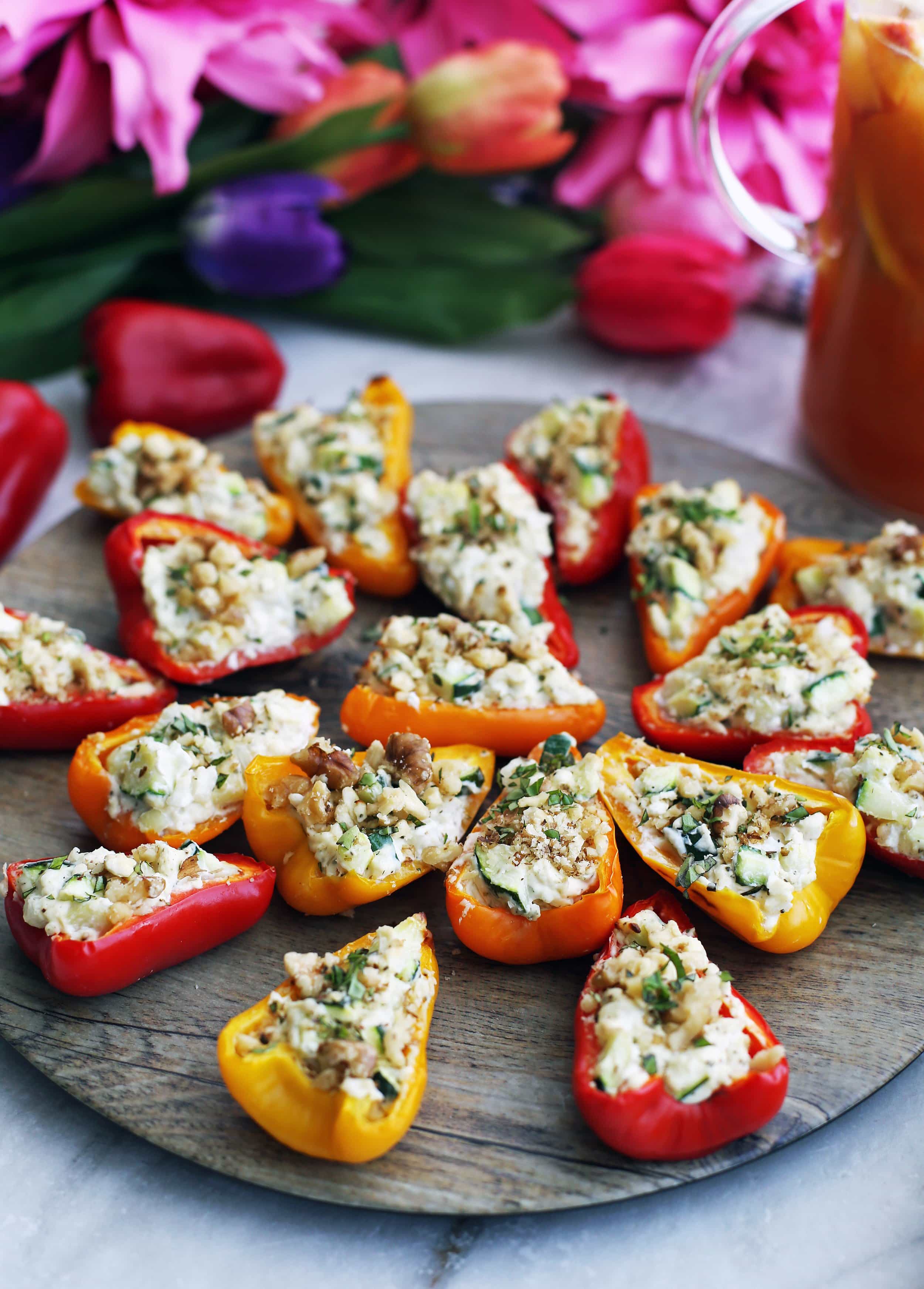 Baked mini bell peppers halves filled with a zucchini, onion, and cream cheese filling on a round wooden platter.