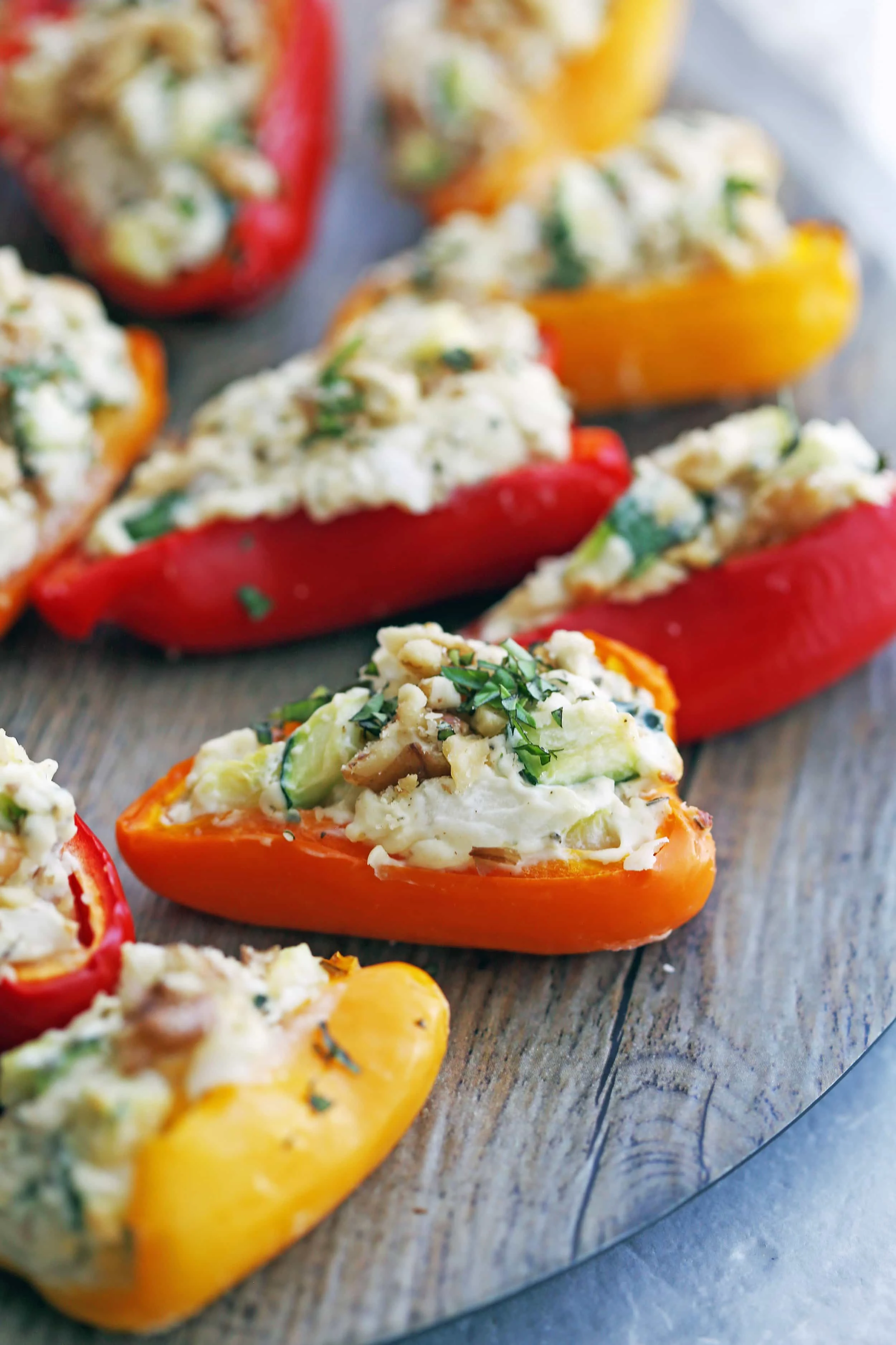 A closeup of a zucchini cream cheese mini bell pepper topped with chopped walnuts and basil on a wooden platter.